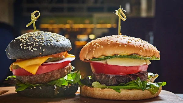 Set med hemlagade hamburgare i svarta och vita bullar med tomat, sallad, ost, lök på trä som serverar styrelsen över mörka bordet. Rustik stil. Hemmagjord snabbmat. — Stockfoto