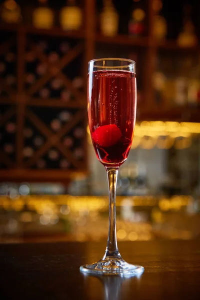Czerwony koktajl w szampan szkło w pobliżu w pasku z niesamowite tło zamazane. — Zdjęcie stockowe