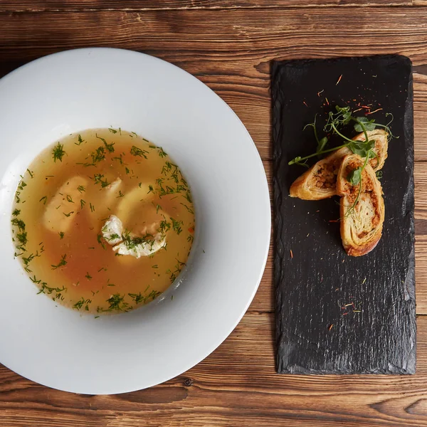 Beautiful presentation of the fish soup in a white plate, with bread on a wooden background