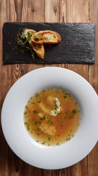 Hermosa presentación de la sopa de pescado en un plato blanco, con pan sobre un fondo de madera — Foto de Stock