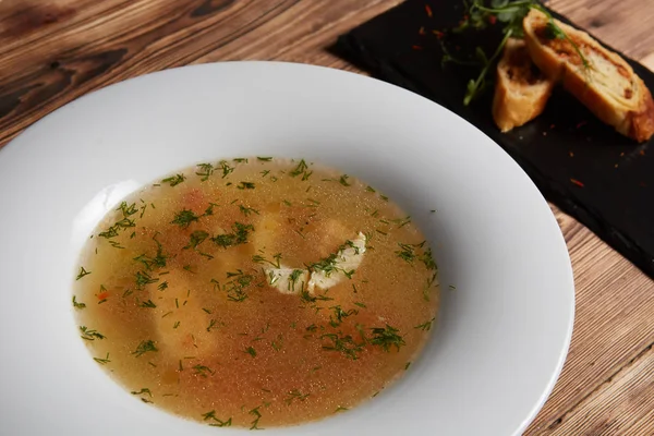 Hermosa presentación de la sopa de pescado en un plato blanco, con pan sobre un fondo de madera —  Fotos de Stock