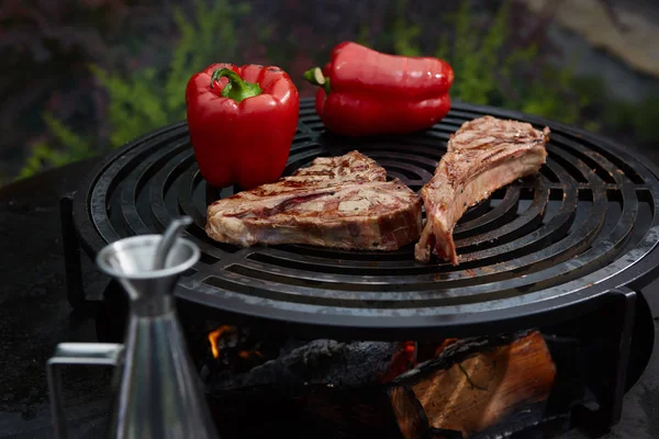 Tomahawk rib beef steak and T-bone on hot black grill.