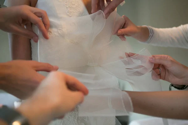 Mãos de namoradas ajudando a noiva a vestir seu vestido — Fotografia de Stock