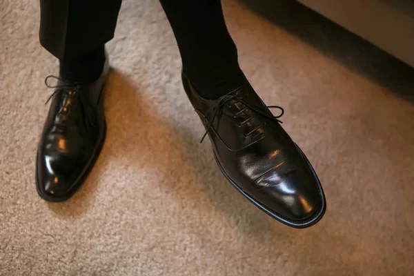Vista de cerca de las manos del novio poniéndose los zapatos negros brillantes mientras está sentado en la cama . —  Fotos de Stock