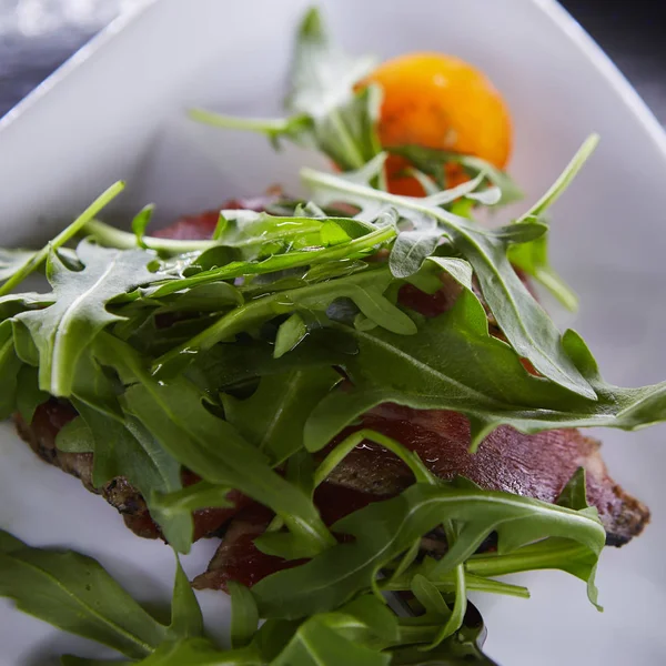 Slice of prosciutto or jamon with arugula leafs — Stock Photo, Image