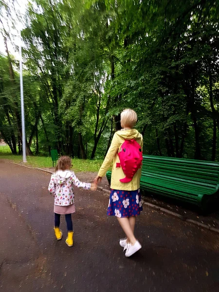 Mother and little curly toddler girl walking together in a park on a wet summer day after rain, view from the back — Stock Photo, Image