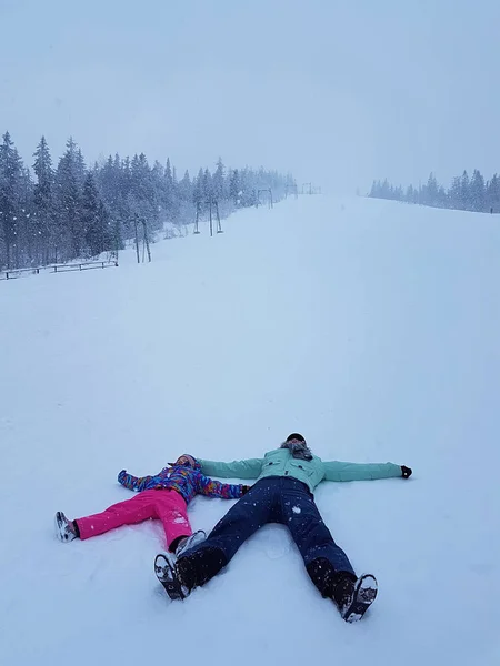 Tochter und Mutter spielen und liegen im Winter draußen im Schnee — Stockfoto