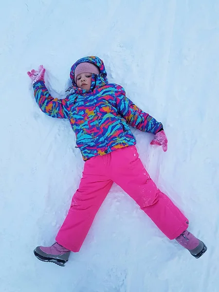 Χαριτωμένο παιδί κοριτσάκι σε θερμή σκι σπορ ταιριάζει κάνοντας άγγελος χιονιού σε εξωτερικούς χώρους. Το παιδί έχοντας διασκέδαση ξαπλωμένος σε χιονοστιβάδα μετά την καταιγίδα χιόνι τον χειμώνα. Υπαίθριες δραστηριότητες τα παιδιά. Χειμερινές διακοπές και αργίες. — Φωτογραφία Αρχείου