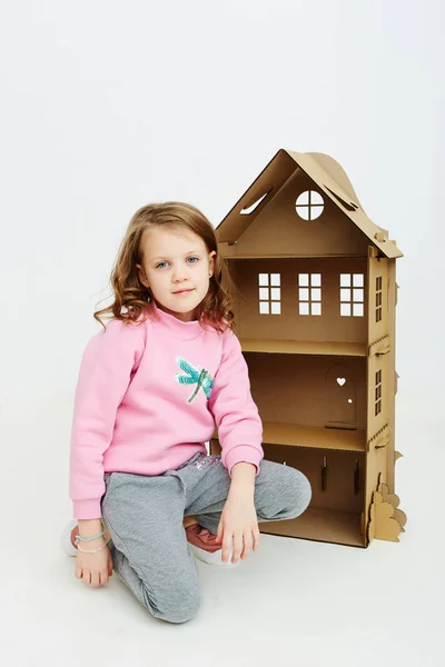 Happy girl plays with cardboard doll house. Funny lovely child is having fun. — Stock Photo, Image