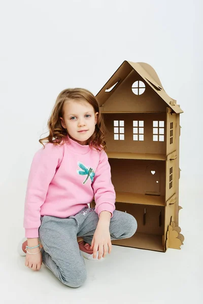 Happy girl plays with cardboard doll house. Funny lovely child is having fun. — Stock Photo, Image