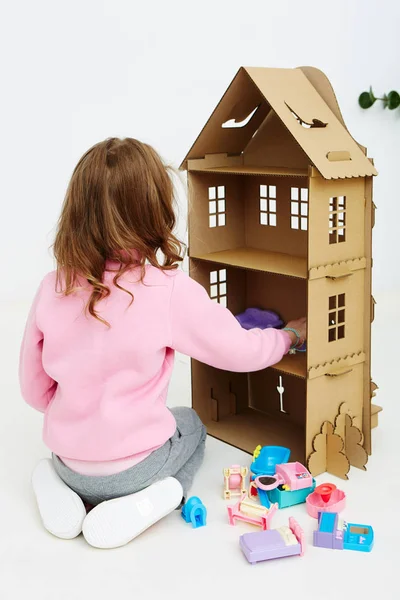 Szczęśliwy dziewczyna gra z tekturowym domu lalki. Śmieszne piękne dziecko jest zabawy. — Zdjęcie stockowe