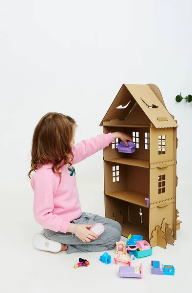 Chica feliz juega con casa de muñecas de cartón. Divertido niño encantador se está divirtiendo . —  Fotos de Stock