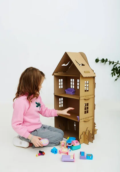 Happy girl plays with cardboard doll house. Funny lovely child is having fun. — Stock Photo, Image