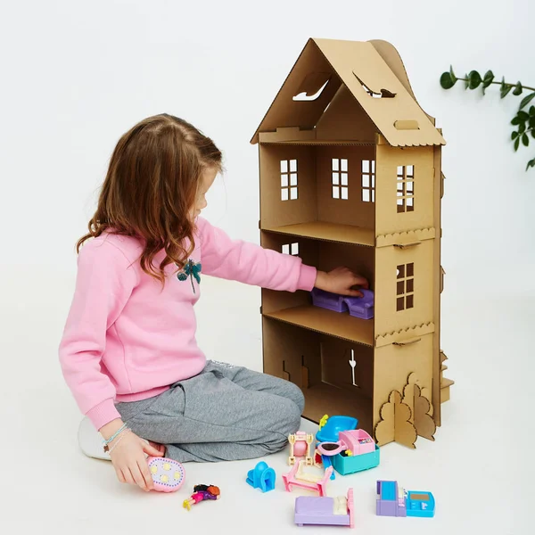 Happy girl plays with cardboard doll house. Funny lovely child is having fun. — Stock Photo, Image