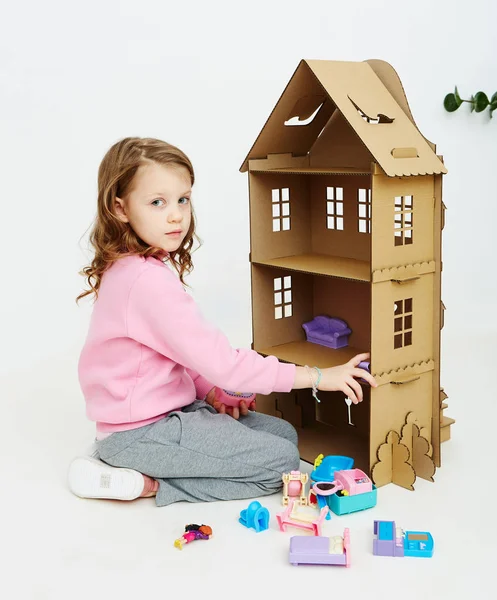 Chica feliz juega con casa de muñecas de cartón. Divertido niño encantador se está divirtiendo . —  Fotos de Stock