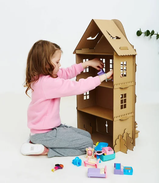 Szczęśliwy dziewczyna gra z tekturowym domu lalki. Śmieszne piękne dziecko jest zabawy. — Zdjęcie stockowe