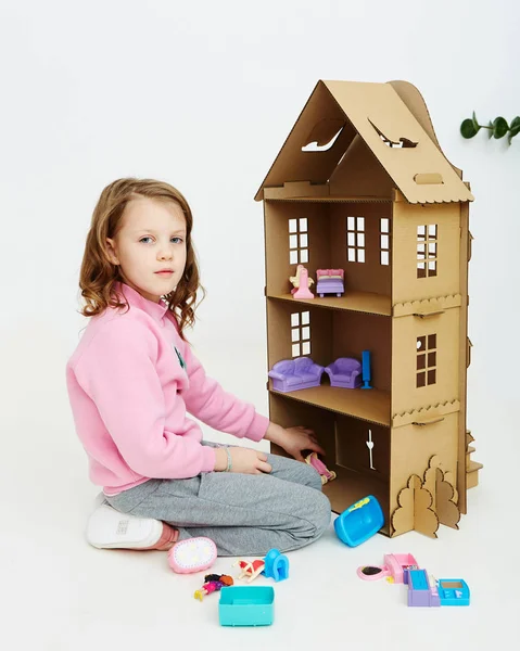 Happy girl plays with cardboard doll house. Funny lovely child is having fun. — Stock Photo, Image