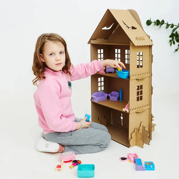 Happy girl plays with cardboard doll house. Funny lovely child is having fun. — Stock Photo, Image