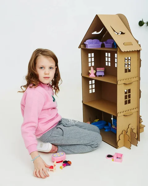 Happy girl plays with cardboard doll house. Funny lovely child is having fun. — Stock Photo, Image