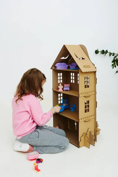 Happy girl plays with cardboard doll house. Funny lovely child is having fun. — Stock Photo, Image