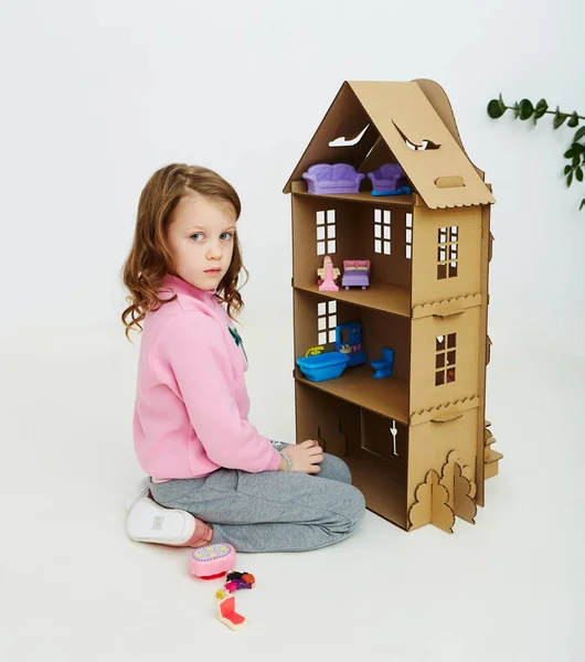Happy girl plays with cardboard doll house. Funny lovely child is having fun. — Stock Photo, Image