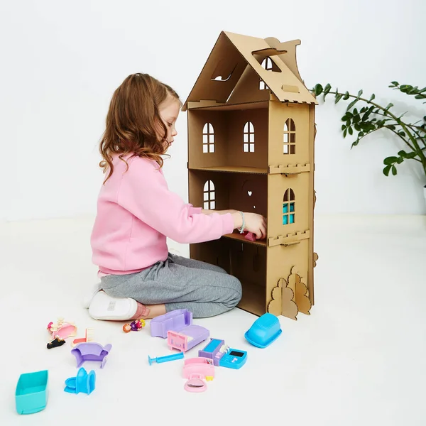 Chica feliz juega con casa de muñecas y muebles de casa de muñecas. Divertido niño encantador se está divirtiendo . —  Fotos de Stock