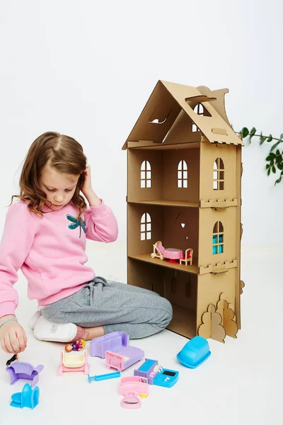 Happy girl plays with doll house and doll house furniture. Funny lovely child is having fun. — Stock Photo, Image