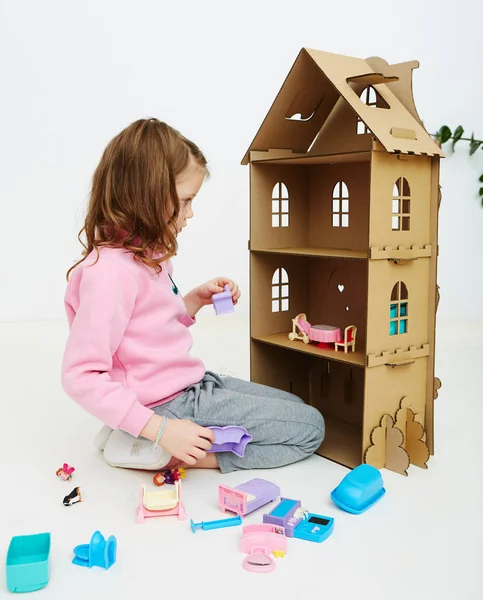 Chica feliz juega con casa de muñecas y muebles de casa de muñecas. Divertido niño encantador se está divirtiendo . —  Fotos de Stock
