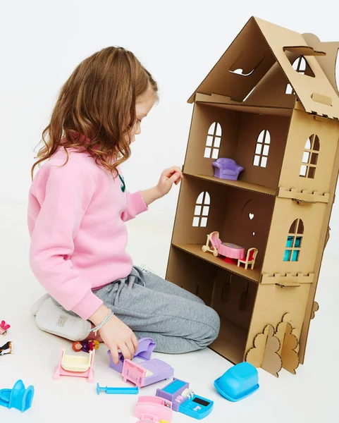 Happy girl plays with doll house and doll house furniture. Funny lovely child is having fun. — Stock Photo, Image