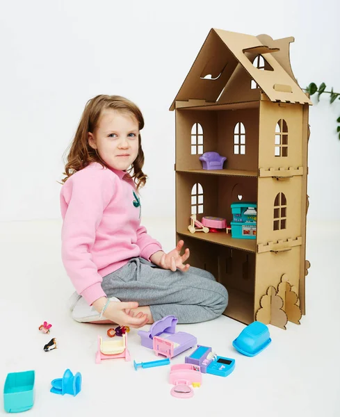 Happy girl plays with doll house and doll house furniture. Funny lovely child is having fun. — Stock Photo, Image