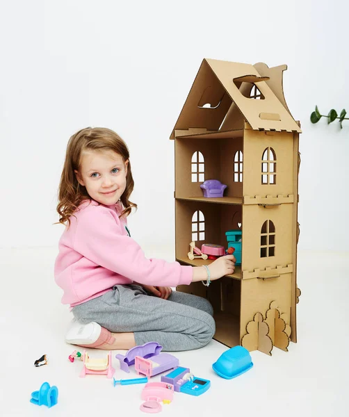 Happy girl plays with doll house and doll house furniture. Funny lovely child is having fun. — Stock Photo, Image