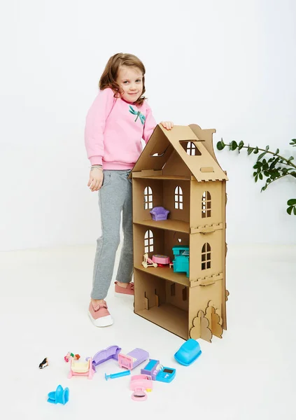 Happy girl plays with doll house and doll house furniture. Funny lovely child is having fun. — Stock Photo, Image