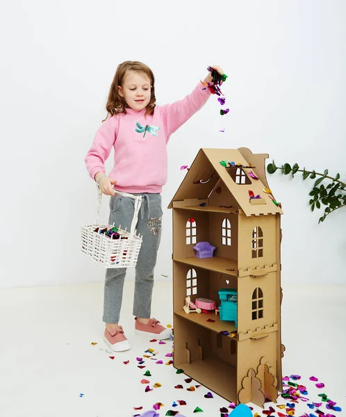 Happy beautiful little girl enjoying colorful confetti surprise falling down, posing on white studio wall. Pretty girl celebrating her birthday party, having fun — Stock Photo, Image