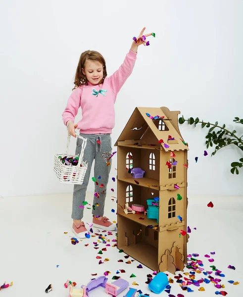 Happy beautiful little girl enjoying colorful confetti surprise falling down, posing on white studio wall. Pretty girl celebrating her birthday party, having fun — Stock Photo, Image