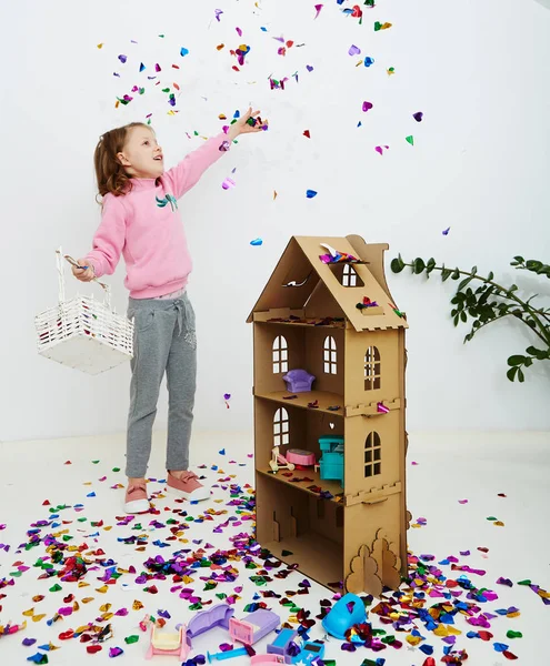 カラフルな紙吹雪驚き落ちて、白いスタジオの壁にポージングを楽しんで幸せな美しい小さな女の子。かわいい女の子の楽しい時を過す彼女の誕生日パーティーを祝う — ストック写真