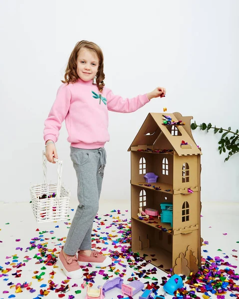 Happy beautiful little girl enjoying colorful confetti surprise falling down, posing on white studio wall. Pretty girl celebrating her birthday party, having fun — Stock Photo, Image