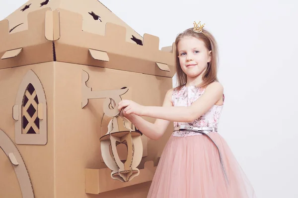 Маленькая принцесса в короне играет со своим картонным замком. Истинное чувство счастья ребенка . — стоковое фото