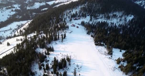 Havadan görünümü. Buzlu çam ormanı kış resort ve kayak yamaçlarına doğru üzerinde uçan. Karlı Kayak Kış Güneşi sessiz Kayak Merkezi yükselen izler — Stok video