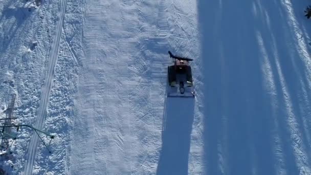 Vista aérea de arriba hacia abajo de un snowcat o un snowgroomer en una pista de esquí en invierno — Vídeos de Stock