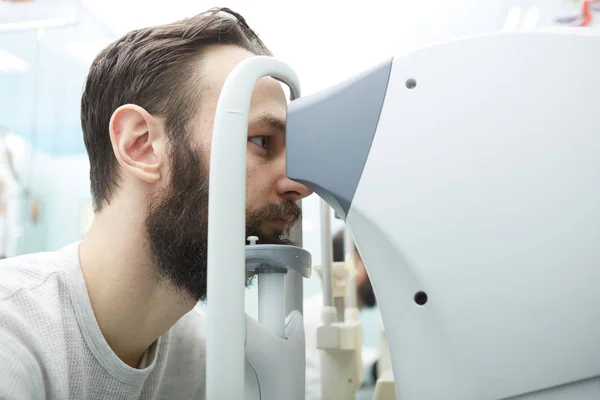 Knappe jongeman is het controleren van de ogen visie in moderne oogheelkunde kliniek. Patiënt in oogheelkunde kliniek. — Stockfoto