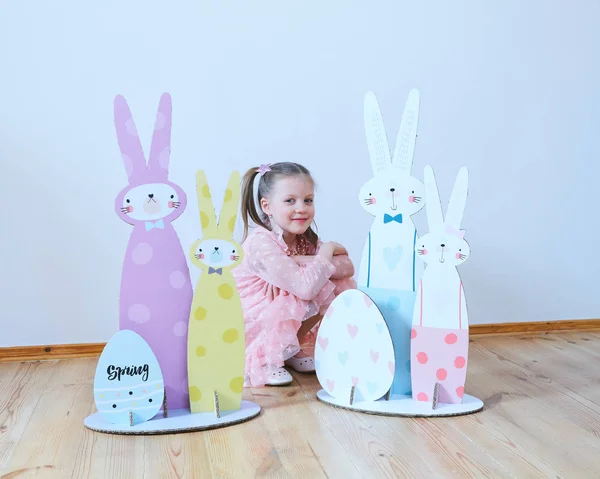 Paskalya 2019 güzel Paskalya süsleri ile elbiseli küçük kız. Büyük Paskalya tavşanları. Bir sürü farklı renkli Paskalya dekor. Çok renkli dekor — Stok fotoğraf