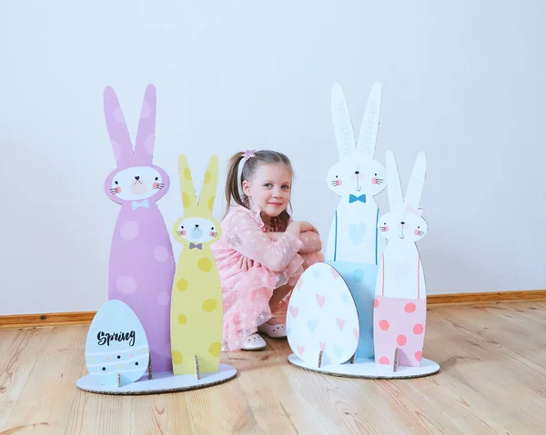 Paskalya 2019 güzel Paskalya süsleri ile elbiseli küçük kız. Büyük Paskalya tavşanları. Bir sürü farklı renkli Paskalya dekor. Çok renkli dekor — Stok fotoğraf
