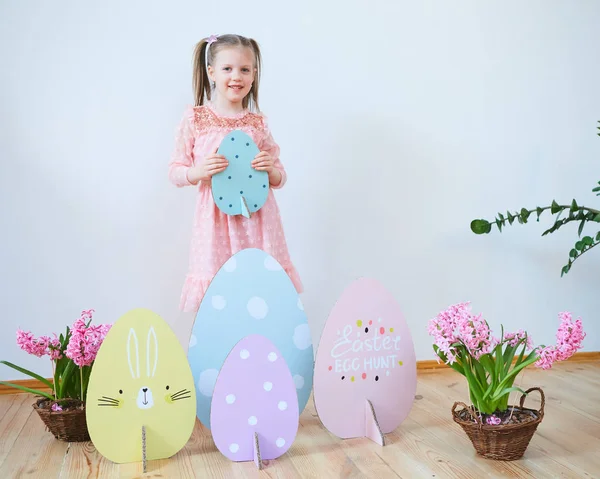 Paskalya 2019 güzel Paskalya süsleri ile elbiseli küçük kız. Büyük Paskalya yumurtaları ve bunnies, renkli bir yer. Bir sürü farklı renkli Paskalya yumurtaları. Çok renkli dekor — Stok fotoğraf