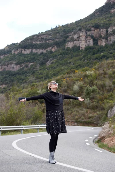 Moda giovane donna in posa su strada asfaltata vuota in montagna — Foto Stock