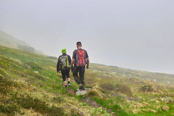 Fog on mountain. Climbers walking down grassy rocky hill in green beautiful mountains. Tourists breathtaking view amazing nature healthy lifestyle, valley of flower — Stock Photo, Image