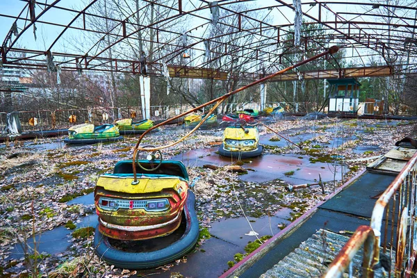 Viejos coches amarillos radiactivos metálicos oxidados rotos, coches eléctricos infantiles, abandonados entre la vegetación, el parque de la cultura y la recreación en la ciudad de Pripyat, el desastre de Chernobyl, Ucrania . — Foto de Stock