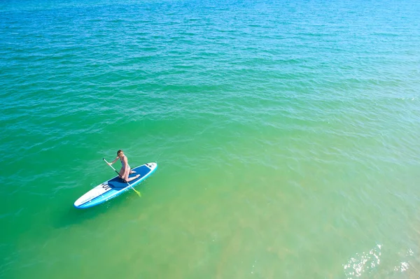 Young woman paddling on SUP board on the tropical beach. Active summer vacations with paddle board. — Stock Photo, Image