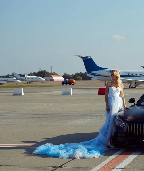 La elegante rubia hermosa mujer posando cerca de vehículo de lujo en los planos de fondo. Chica vistiendo vestido azul. Sin retoque . — Foto de Stock