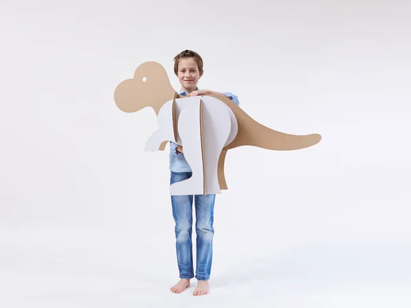 Pequeño niño soñador jugando con un dinosaurio de cartón Tyrannosaurus rex. Infancia. Fantasía, imaginación . — Foto de Stock