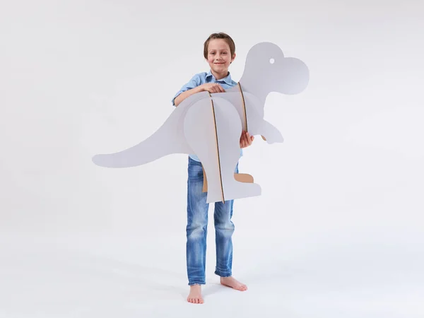 一个梦想中的小男孩和一只硬纸板恐龙霸王龙在一起玩耍。童年。幻想、想象. — 图库照片